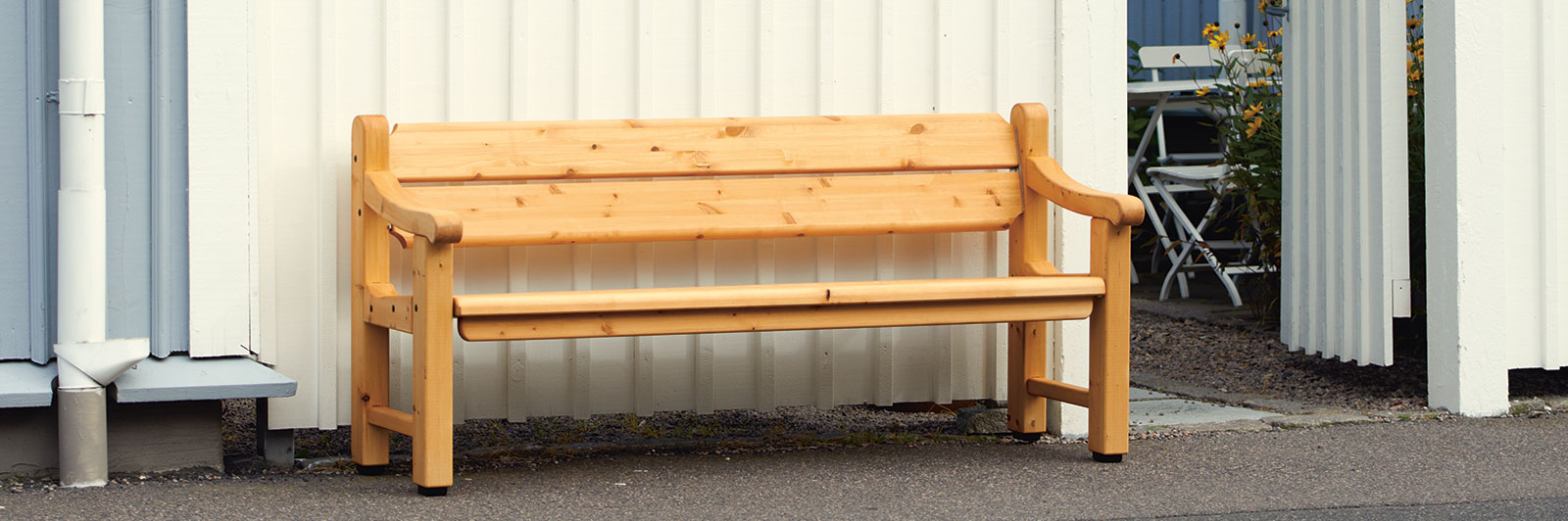 Sehr traditionelle Parkbank aus Holz mit Rückenlehne und Armlehnen an einer Straße.